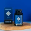 Een flesje MindScopic - CLEAR FOCUS™ Capsules (50 stuks) met een blauw etiket staat op een houten dienblad naast de bijbehorende doos, tegen een blauwe achtergrond.