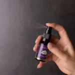 Een hand spuit een klein flesje met de tekst "MindScopic - SLEEPWELL SPRAY met melatonine (15ml)" tegen een donkere achtergrond.