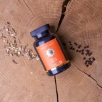 Een flesje MindScopic - MOODMASTER™ capsules (50 stuks) staat op een houten oppervlak, met in de buurt kleine stapeltjes zaden en gedroogde kruiden.