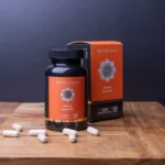Een fles en doos met het opschrift "MindScopic - MOODMASTER™ capsules (50 stuks)" met capsules verspreid over een houten oppervlak, tegen een donkere achtergrond.