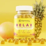 Een potje Harmony - CBD / CBG Relax Gummies (60 stuks) - THT datum 21-11-2025 is afgebeeld met gummies vooraan, een mango links en een ananas rechts, alles tegen een gele achtergrond.