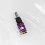 Een klein bruin sprayflesje met de tekst "MindScopic - SLEEPWELL SPRAY met melatonine (15ml)" met een paars en gouden ontwerp staat op een wit, waterig oppervlak.