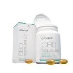 Naast de doos staat een witte fles met het opschrift „CBD-capsules 2.0”, met daarvoor drie gouden capsules. Op de verpakking staat het merk „cibdol”.