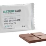 Een witte verpakking van een Naturecan-melkchocoladereep met CBD, met daarvoor vier stukjes chocolade.